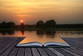 pic of reflection  - Creative concept of beautiful simple image of sunset through tress reflected in lake in foreground coming out of magical book laid open - JPG 