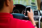 foto of man  - Asian man sitting in car with mobile phone in hand texting while driving - JPG 
