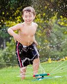 pic of kid  - Young boy or kid cools off by playing in water sprinkler at home in his back yard on hot summer day - JPG 