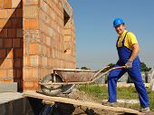 pic of construction worker  - Construction worker wearing blue overall and helmet going inside unfinished brick wall building with wheel - JPG 