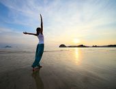 image of sand  - Young woman with raised hands standing on wet sand and looking to a sky - JPG 