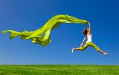 picture of health  - Beautiful young woman jumping on  a green meadow with a colored tissue - JPG 