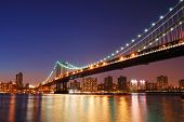 stock photo of bridge  - New York City Manhattan Bridge over Hudson River with skyline after sunset night view illuminated with lights viewed from Brooklyn - JPG 