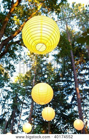 Picture or Photo of Yellow wedding decorations hang from the trees at a wedding ceremony and reception outdoors in Oregon. These yellow chinese lanterns or japanese lantersn are well lit.