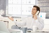 image of call  - Smiling businessman sitting at office desk on landline phone call - JPG 