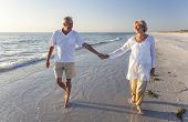 stock photo of beach  - Happy senior man and woman couple walking and holding hands on a deserted tropical beach with bright clear blue sky - JPG 