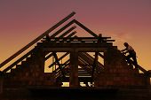 stock photo of construction worker  - Construction worker working with house wooden roof against sunset sky - JPG 