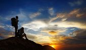 stock photo of sunset  - Silhouettes of two tourists with backpacks relaxing on top of a mountain and enjoying sunset view - JPG 