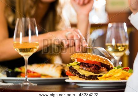 Picture or Photo of Couple - man and woman - in a fine dining restaurant they eat fast food, burger and fries, closeup
