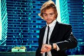 stock photo of pressure  - Young business man standing in the big city and looking at his wristwatch - JPG 