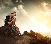 stock photo of sunset  - Young tourist with backpack relaxing on rock and enjoying sunset - JPG 