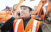 picture of construction  - road construction worker using mobilephone standing in front of excavator - JPG 