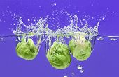image of global technology  - Three Brussels sprouts falling in water on blue with air bubbles - JPG 