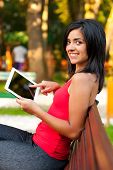 pic of outdoor  - Pretty girl outdoors sitting and showing on her touchcreen tablet - JPG 