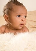 foto of infants  - Thoughtful biracial mix of Hispanic and African American infant lying down on fur and yellowish colored blanket - JPG 