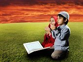 stock photo of religion  - Two Muslims children sitting on meadow in Ramadan and reading Koran and praying - JPG 