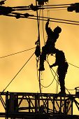 foto of construction worker  - A silhouetted construction workers fix lines on rigging at sunset - JPG 