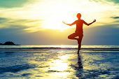 foto of beach  - Woman practicing yoga on the beach at sunset - JPG 