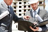stock photo of construction worker  - Portrait of two builders standing at building site and discussing new project held by one of them - JPG 