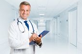 foto of medical doctors  - Happy smiling mature doctor writing on clipboard in a modern hospital - JPG 