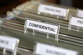stock photo of confidential  - Inside of a filing cabinet with green folders and focus on confidential label - JPG 