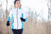 picture of health  - Running young Asian woman jogging in a winter fleece and gloves in open countryside with copyspace in a health and fitness concept - JPG 