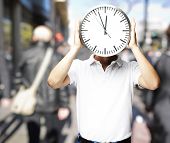 stock photo of watch  - portrait of a man holding a big clock in front of his head at a crowded place - JPG 