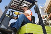 stock photo of industrial  - Low angle view of a confident male industrial worker driving forklift at workplace - JPG 