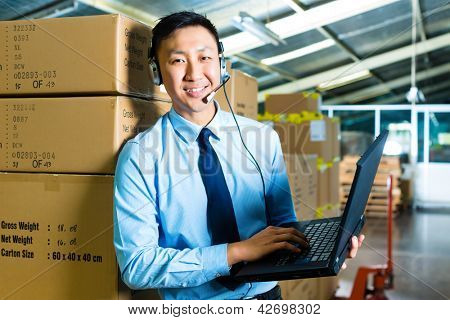 Picture or Photo of Young man in a suit with headset and laptop in a warehouse, he is from the Customer Service