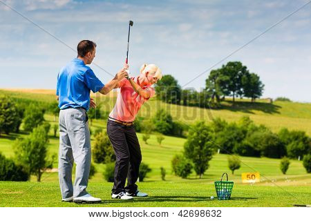 Picture or Photo of Young female golf player at Driving Range with a Golf Pro, she presumably does exercise