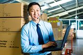 stock photo of laptop  - Young man in a suit with headset and laptop in a warehouse - JPG 