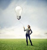 stock photo of wire  - Black girl in a large grace field holding with a wire a big bulb in the air - JPG 