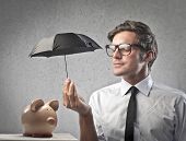 picture of businessmen  - Businessman protecting a piggy with a little black umbrella - JPG 