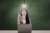 stock photo of technology concept  - Beautiful businesswoman under a lit light bulb while working with her laptop - JPG 