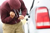 picture of order  - View down the side of a car to a man in a hooded top breaking into a car with a screwdriver in order to steal it - JPG 
