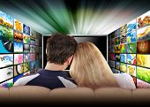 picture of  photo  - A couple is sitting on a couch watching a flat screen television with photo images coming out of the sides - JPG 