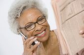 foto of newspaper  - Happy African American senior woman reading newspaper while using cell phone - JPG 