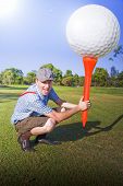 stock photo of golf  - Lifestyle Sports Image Of A Golfer Bending Down On A Golf Course Fairway Holds A Gigantic Golf Ball And Tee In A Funny And Humorous Expression Of Big Golf - JPG 