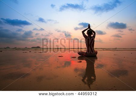 Picture or Photo of Silhouette young woman practicing yoga on the beach at sunset