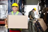 image of mid adult  - Portrait of happy mid adult foreman with cardboard box and coworker pushing handtruck at warehouse - JPG 