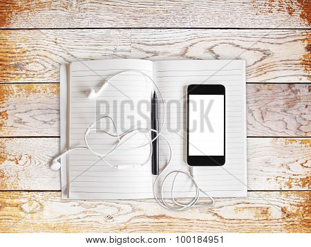Blank Cell Phone With Headhones And Diary On A Wooden Table