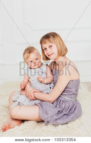 Baby girl sits on her older sisters knees
