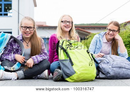 Schoolgirls sitting in schoolyard at school having recess and talking