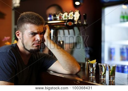 Young drunk man drinking tequila in bar