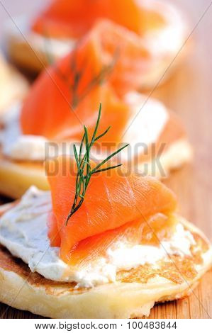 Gourmet smoked salmon and cream cheese blinis on a wooden platter 