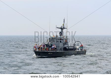 KOLOBRZEG - AUGUST 12: Tourists enjoying the sunny weather and a cruise military ship on the sea on 12 August 2015 in Kolobrzeg, Poland. It is an old military frigate converted into a tourist ship.