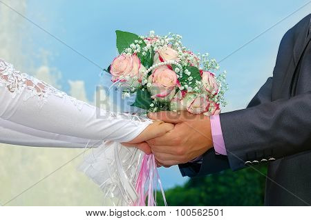 Hands of groom and bride with a wedding bouquet