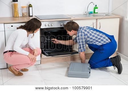 Woman Looking At Worker Repairing Oven