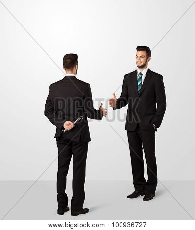 Two opposing businessman shake hands, one of them hiding a weapon behind his back
