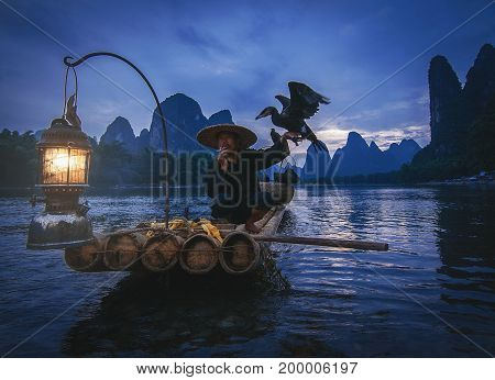 Guilin China; 17th June 2014 - A shot of the famous cormorant taking a smoke break while holding a cormorant bird.